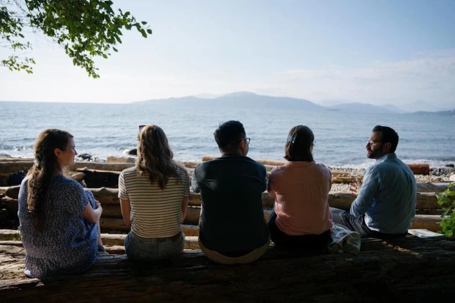 Five students sit side-by-side on a beach, looking across the Burrard Inlet in Vancouver.